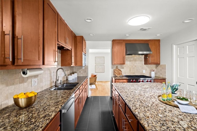 kitchen with stainless steel dishwasher, range hood, dark stone countertops, and a sink