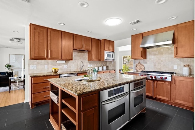 kitchen featuring visible vents, appliances with stainless steel finishes, a sink, wall chimney range hood, and dark tile patterned flooring