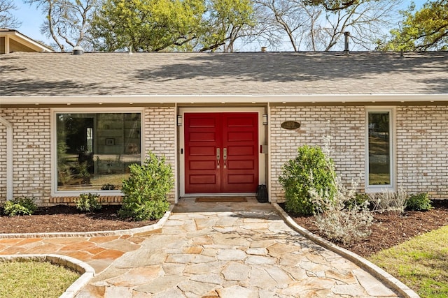 entrance to property with a shingled roof and brick siding