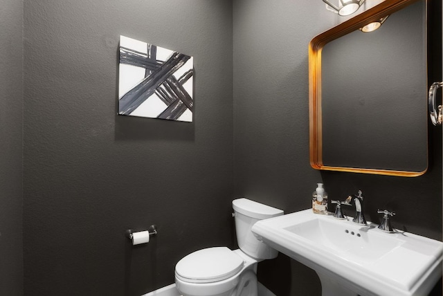 half bath with toilet, a sink, and a textured wall