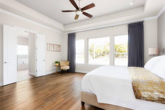 bedroom with ensuite bathroom, baseboards, ornamental molding, wood-type flooring, and a raised ceiling