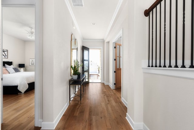 corridor with baseboards, crown molding, visible vents, and hardwood / wood-style floors