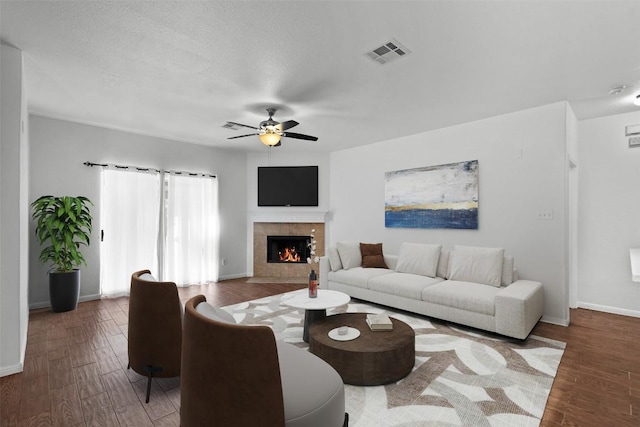 living room featuring visible vents, a tiled fireplace, ceiling fan, wood finished floors, and baseboards