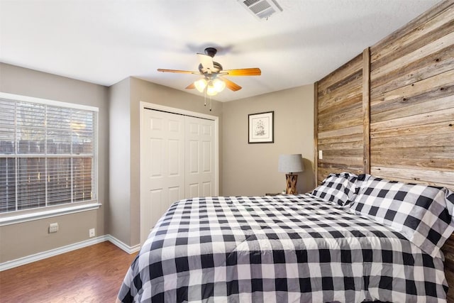 bedroom with baseboards, visible vents, a ceiling fan, wood finished floors, and a closet