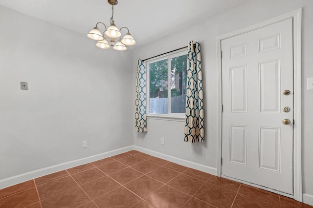 empty room featuring dark tile patterned flooring, baseboards, and an inviting chandelier