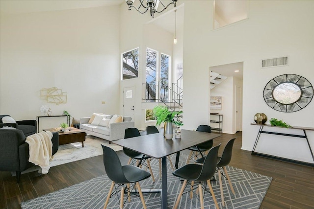 dining room with a towering ceiling, visible vents, stairs, dark wood finished floors, and an inviting chandelier