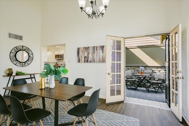 dining room with a notable chandelier, wood finished floors, a towering ceiling, visible vents, and french doors