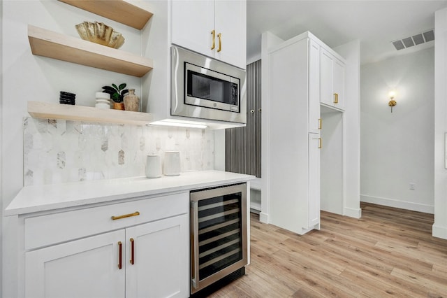 360 Judy Dr, Dripping Springs, TX 78620 - bar with light wood-style flooring, beverage cooler, visible vents, stainless steel microwave, and decorative backsplash