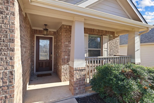 view of exterior entry featuring covered porch and brick siding