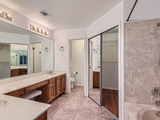 bathroom featuring a textured ceiling, tile patterned flooring, toilet, visible vents, and double vanity