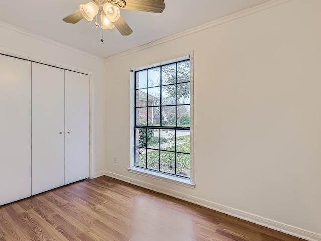 unfurnished bedroom featuring crown molding, multiple windows, baseboards, and wood finished floors