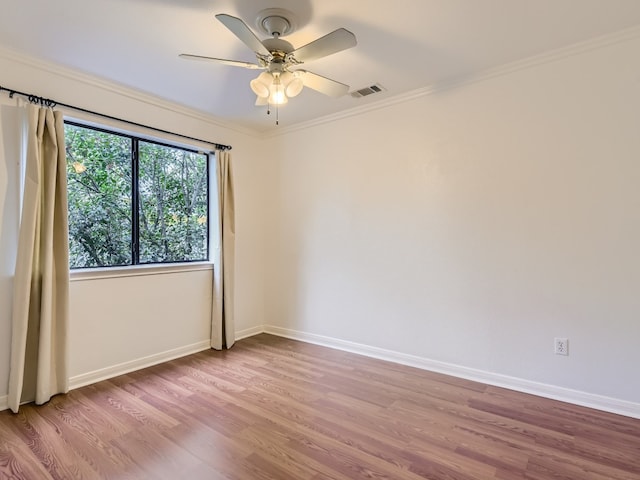 empty room with ornamental molding, visible vents, baseboards, and wood finished floors