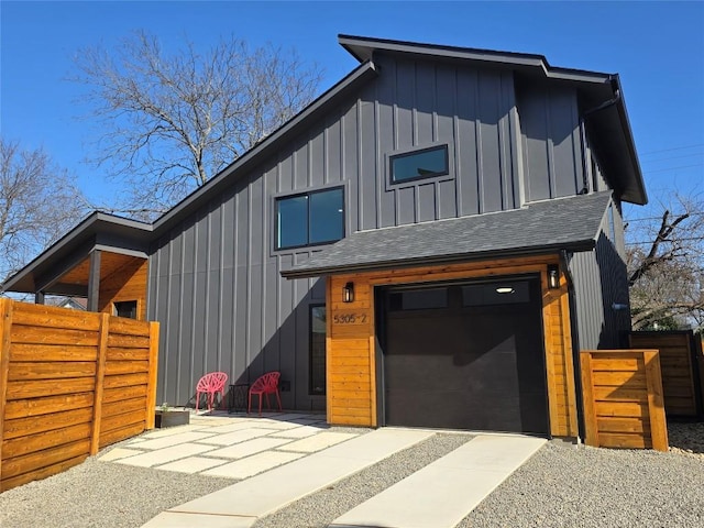 view of front facade with an attached garage, fence, board and batten siding, and roof with shingles