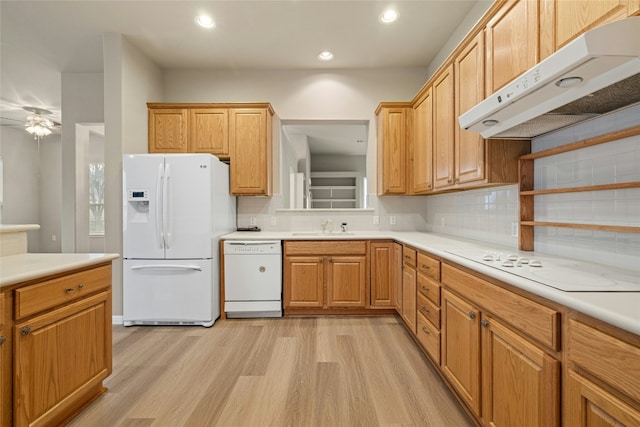 kitchen featuring tasteful backsplash, a sink, light wood-type flooring, white appliances, and under cabinet range hood