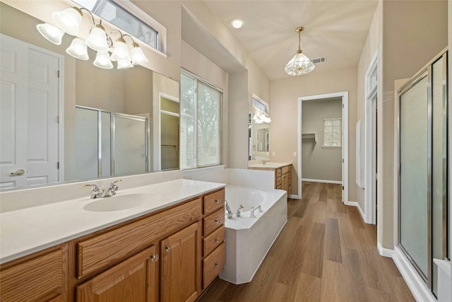 bathroom featuring a garden tub, a notable chandelier, a stall shower, a sink, and wood finished floors