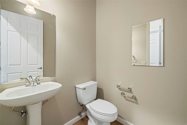 half bath with baseboards, toilet, and wood finished floors