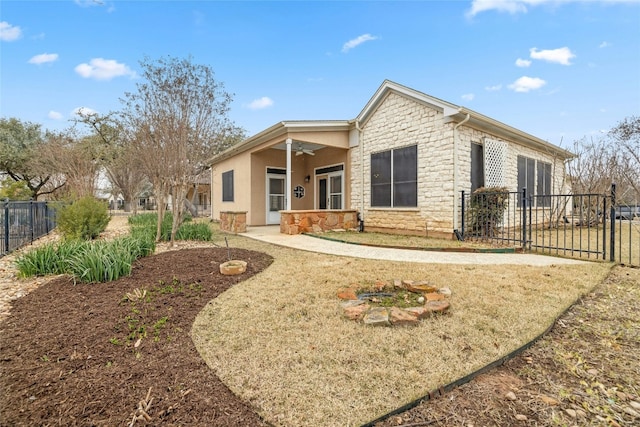 back of house with stone siding, fence, a ceiling fan, and a patio