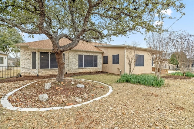 rear view of property featuring stone siding, fence, and stucco siding