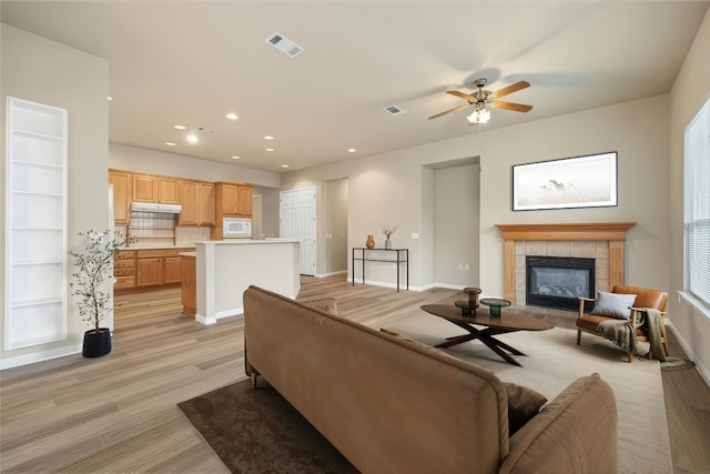 living room featuring light wood-style flooring, recessed lighting, visible vents, baseboards, and a tiled fireplace