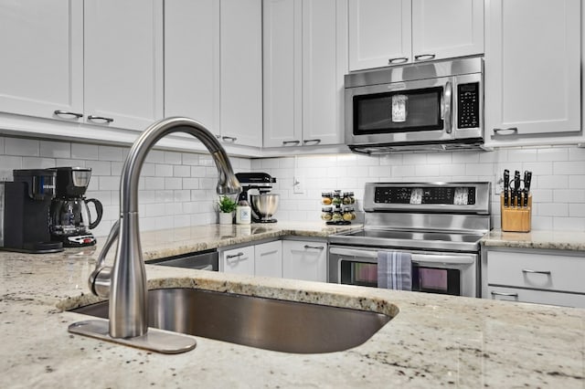 kitchen with stainless steel appliances, decorative backsplash, white cabinets, a sink, and light stone countertops