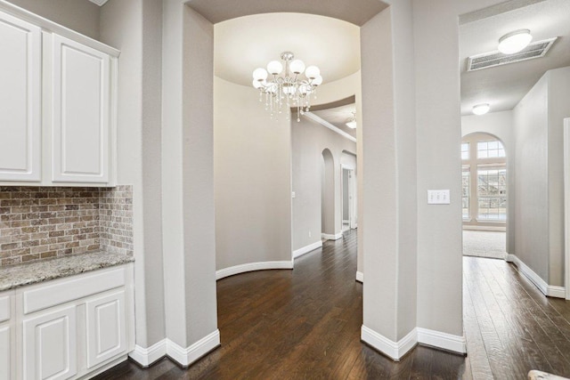 corridor with visible vents, arched walkways, dark wood finished floors, and baseboards