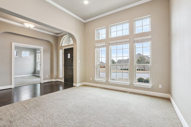 entrance foyer with baseboards, dark wood finished floors, arched walkways, crown molding, and dark carpet