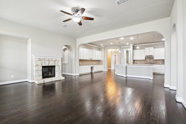 unfurnished living room featuring visible vents, a stone fireplace, dark wood-type flooring, and a ceiling fan