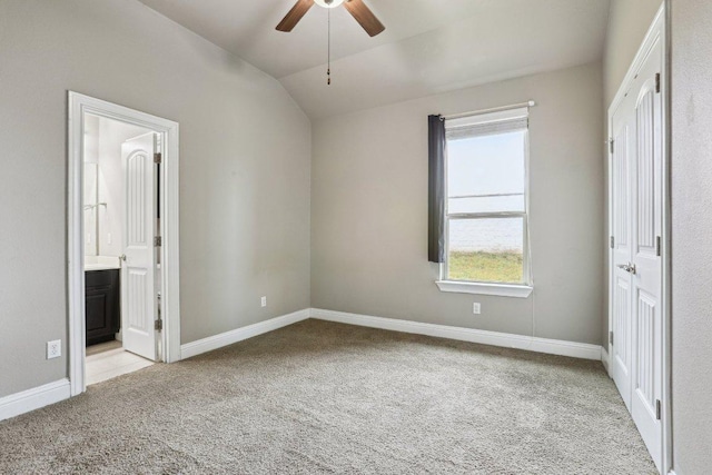 unfurnished bedroom featuring light carpet, baseboards, a ceiling fan, lofted ceiling, and ensuite bath