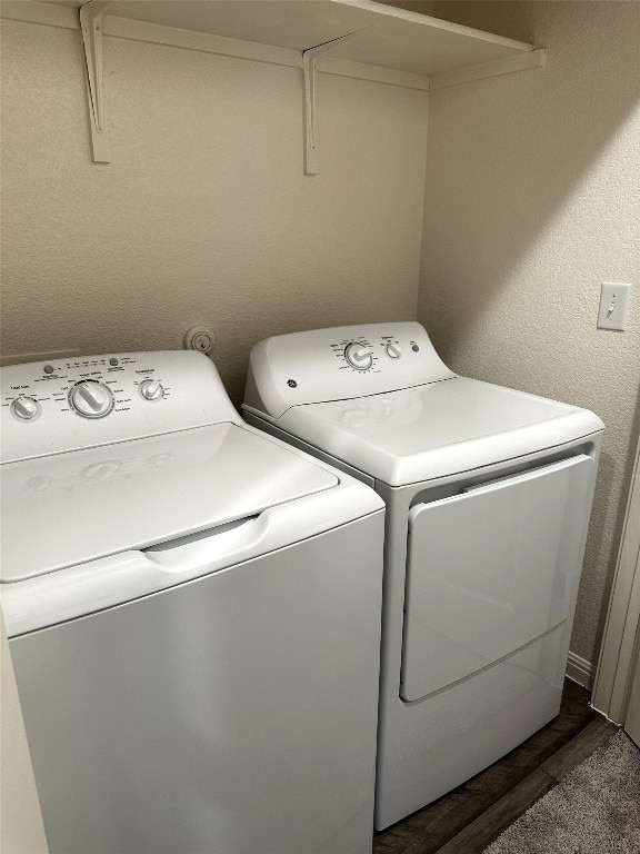 clothes washing area with dark wood-type flooring, laundry area, a textured wall, and washing machine and clothes dryer