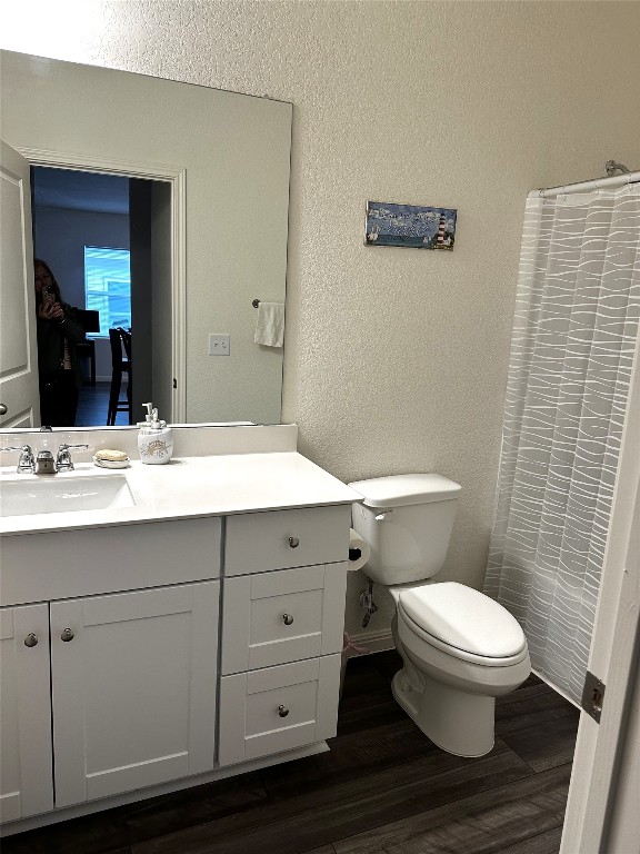 bathroom with baseboards, a textured wall, toilet, wood finished floors, and vanity