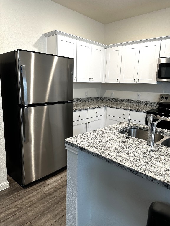 kitchen with appliances with stainless steel finishes, dark wood-style flooring, white cabinets, and light stone counters