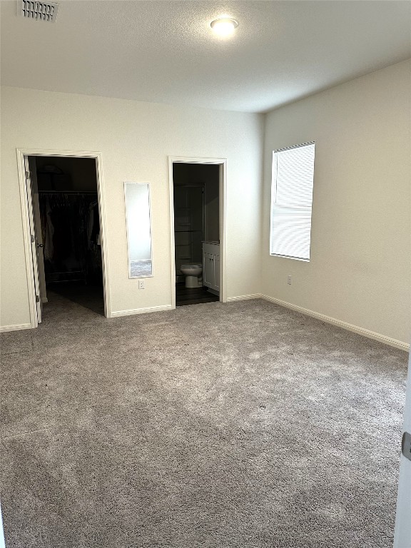 unfurnished bedroom featuring visible vents, a spacious closet, a textured ceiling, carpet floors, and a closet