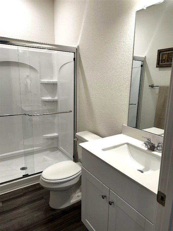 full bathroom with toilet, a shower stall, wood finished floors, and a textured wall