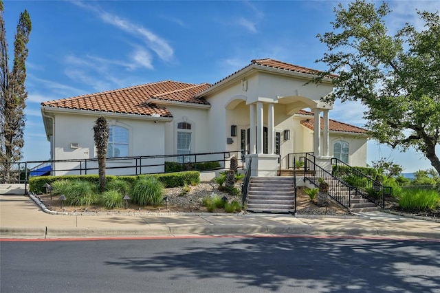 mediterranean / spanish home featuring fence, a tiled roof, and stucco siding