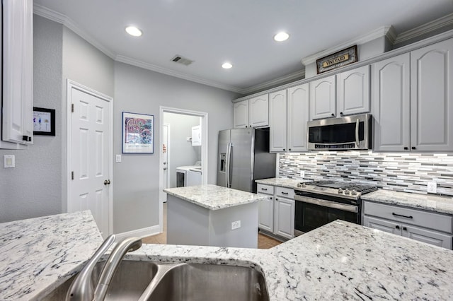 kitchen with visible vents, appliances with stainless steel finishes, ornamental molding, independent washer and dryer, and a sink