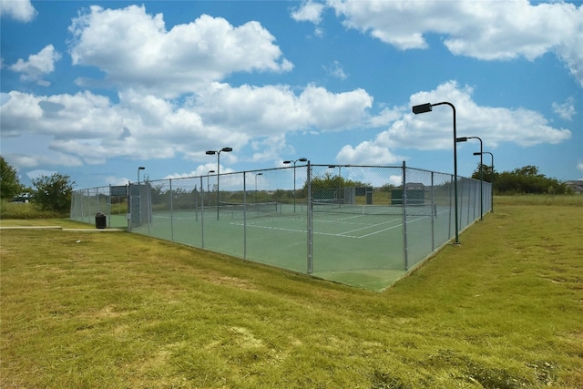 view of tennis court featuring a lawn and fence