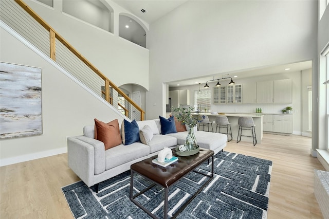 living room with light wood-style floors, arched walkways, baseboards, and stairs