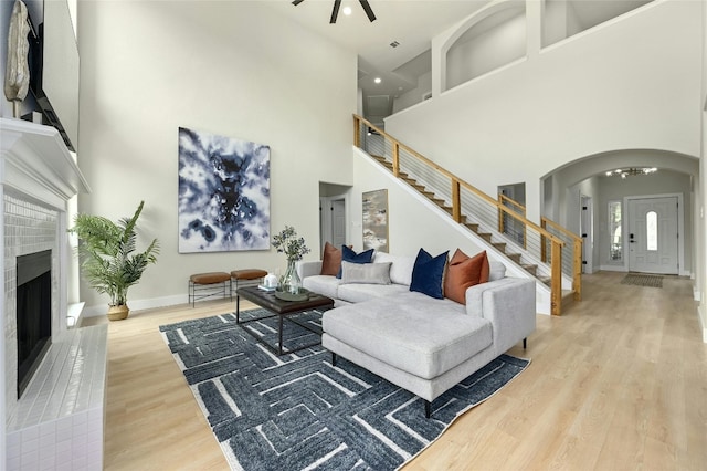 living room featuring baseboards, a fireplace with raised hearth, arched walkways, stairway, and wood finished floors