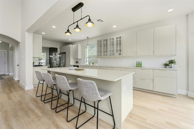 kitchen with visible vents, arched walkways, a kitchen island, freestanding refrigerator, and a kitchen bar