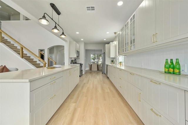 kitchen featuring light wood-style flooring, stainless steel appliances, a sink, visible vents, and backsplash