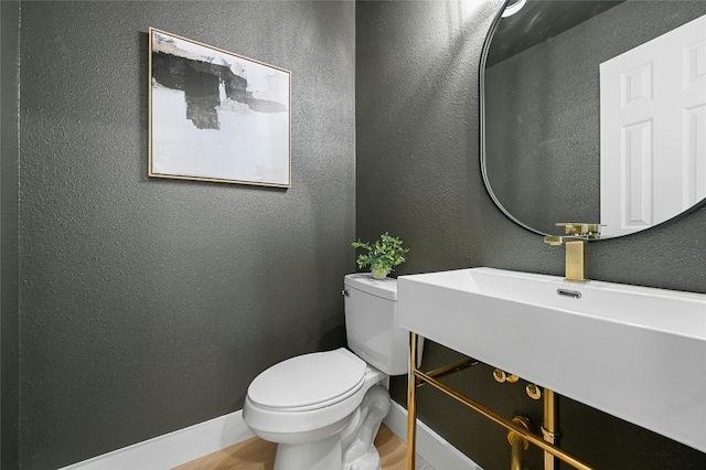 bathroom featuring baseboards, a textured wall, and toilet