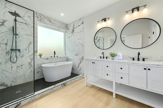 full bath featuring double vanity, a marble finish shower, a sink, and wood finished floors