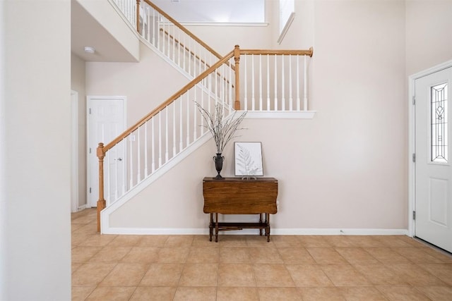 tiled foyer featuring baseboards, a high ceiling, and stairs