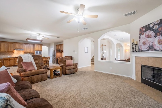 living room featuring a fireplace, light colored carpet, visible vents, a ceiling fan, and baseboards