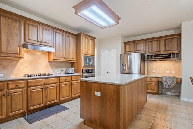 kitchen with under cabinet range hood, appliances with stainless steel finishes, brown cabinetry, and built in study area