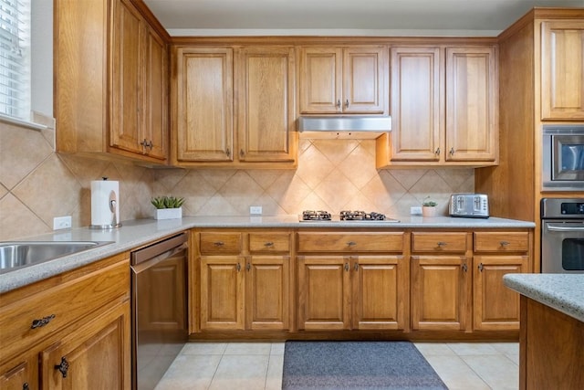 kitchen featuring brown cabinets, tasteful backsplash, light countertops, appliances with stainless steel finishes, and under cabinet range hood