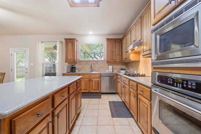 kitchen featuring light tile patterned floors, decorative backsplash, stainless steel appliances, under cabinet range hood, and a sink