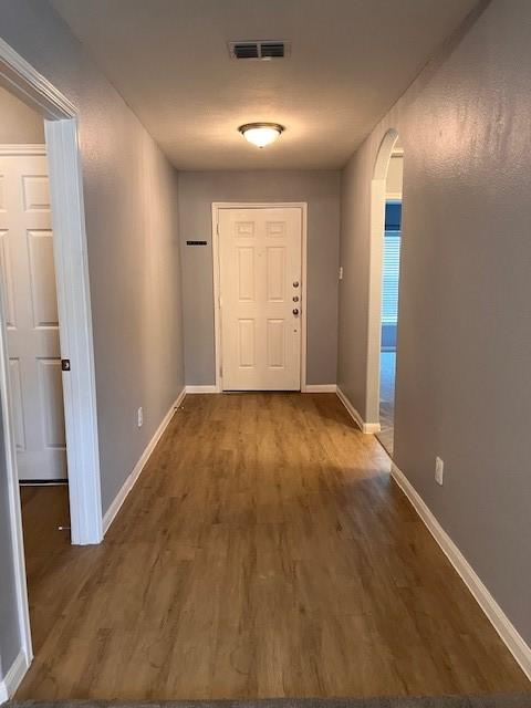 corridor featuring baseboards, visible vents, arched walkways, and wood finished floors