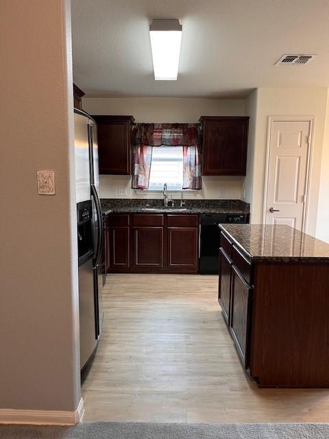 kitchen featuring visible vents, fridge with ice dispenser, a sink, and dark brown cabinets