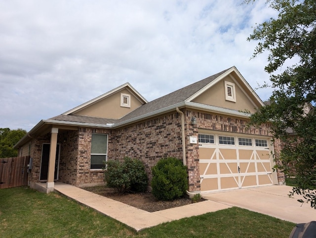 view of front of home with a garage, driveway, brick siding, and stucco siding